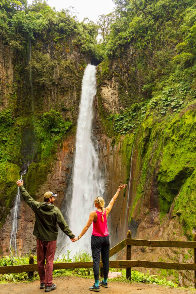 two hikers stand in front of catarata del toro in costa rica