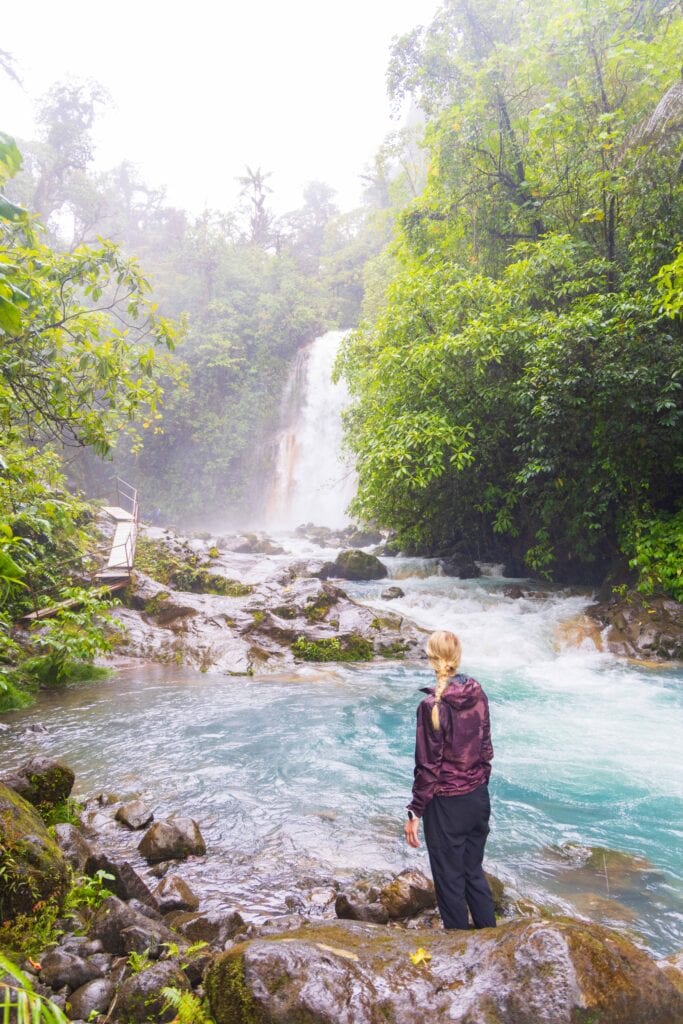 a woman stares at a waterfall in costa rica's blue falls area
