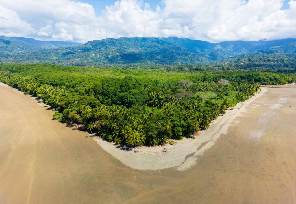 the beach in uvita with sand in the foreground and trees and clouds above