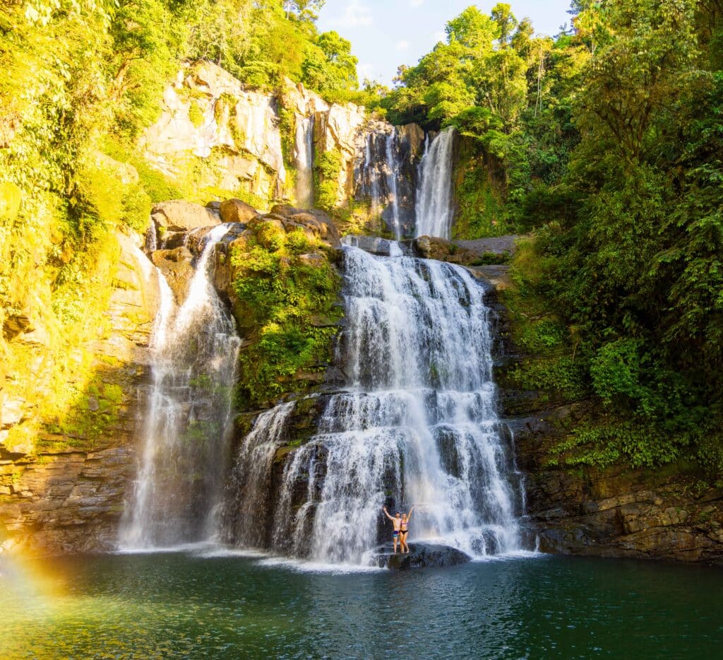 two tourists stand in front of the nauyaca waterfall in costa rica