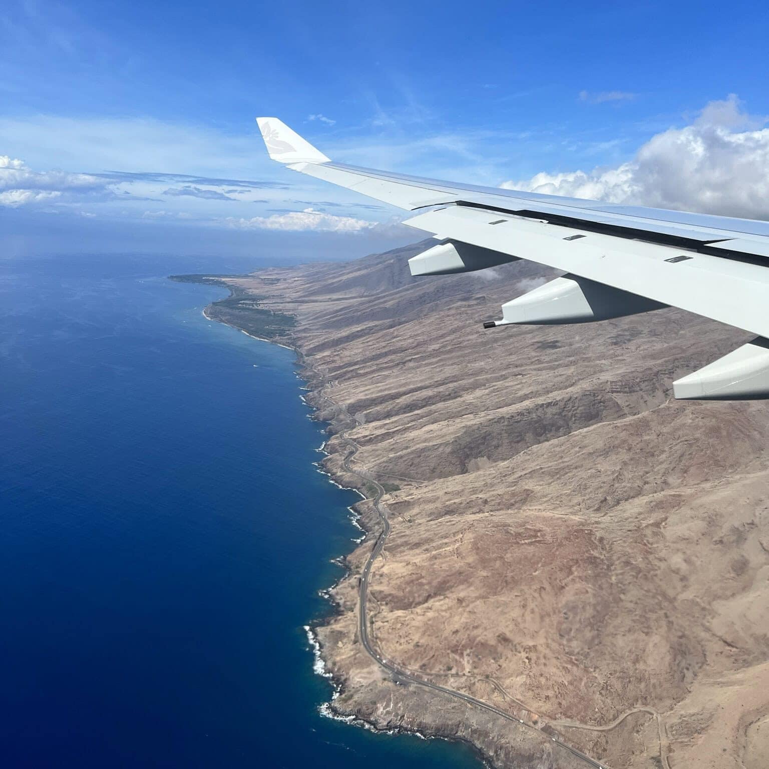 an airplane wing flying over the dry side of maui in hawaii