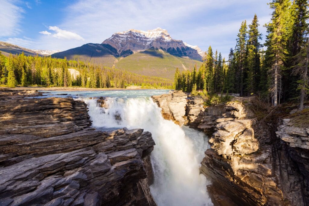 athabasca falls in jasper national park with rocks in the foreground and a big mountain towering above