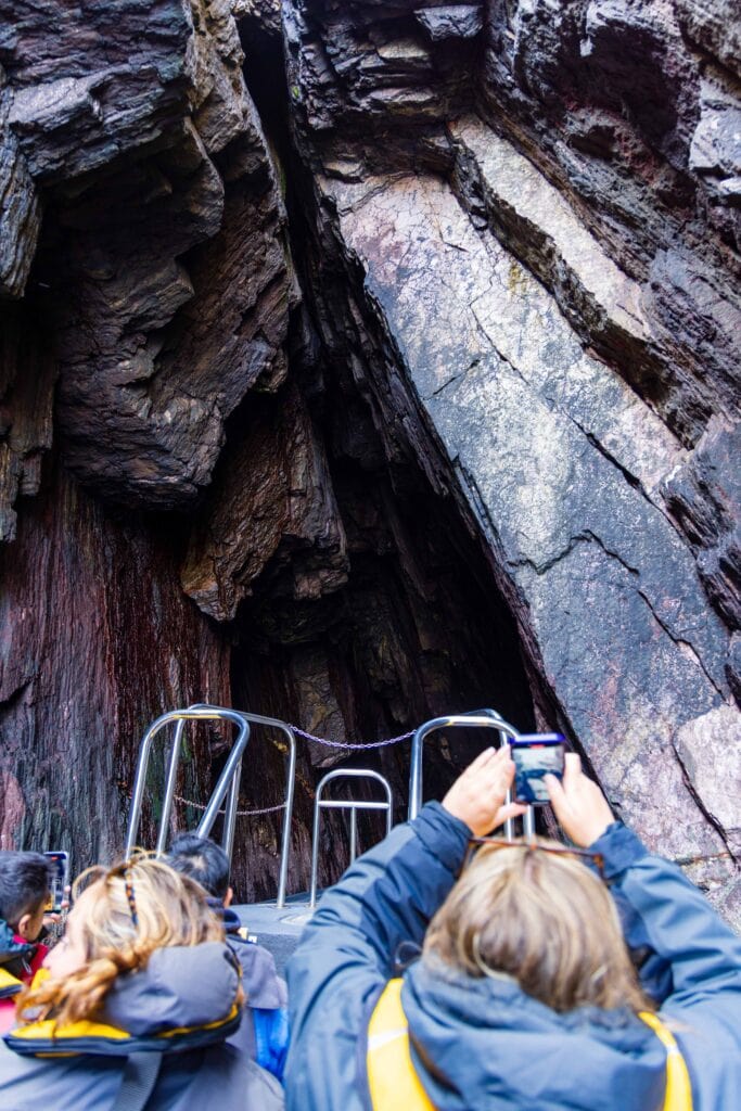 tourist hold up their phones to capture the sea cave and rocks