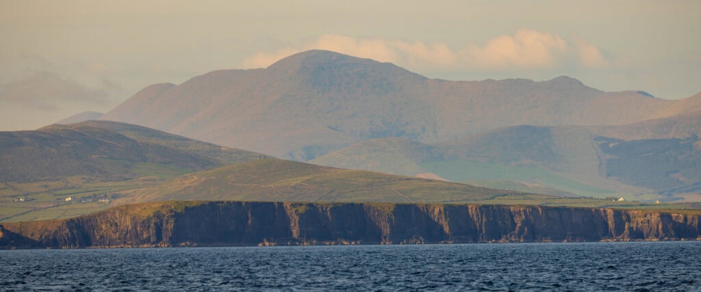 the dingle cliffs with some clouds above it and mountains