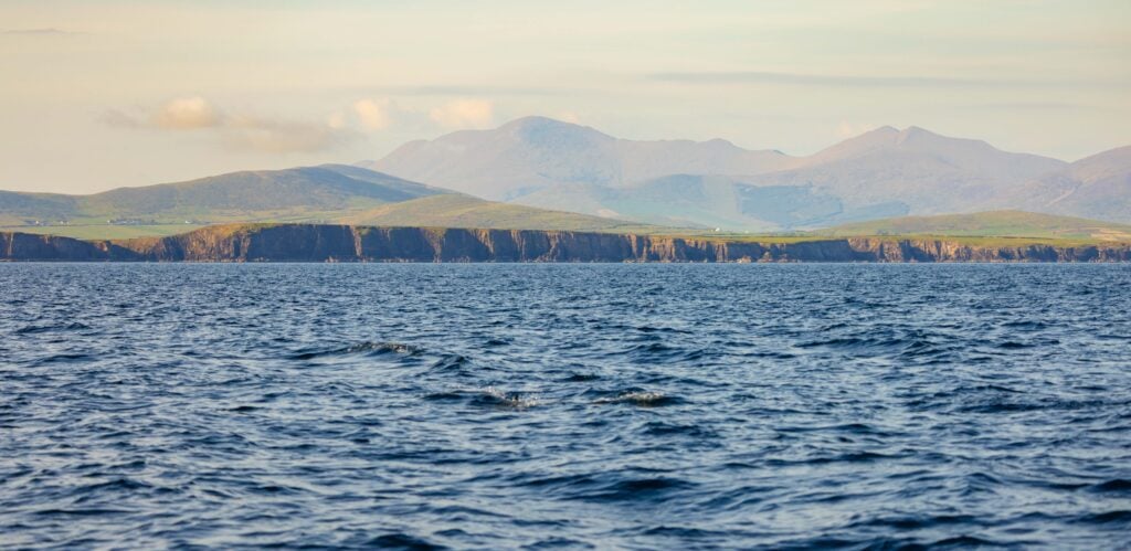 the dingle cliffs with some clouds above it and mountains