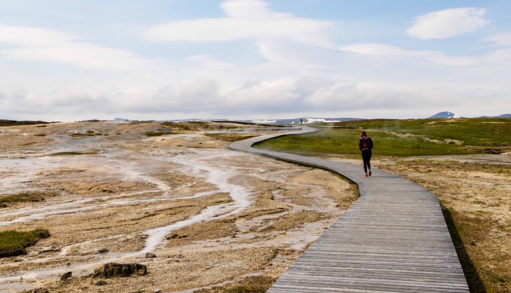 a woman walks on a boardwalk in the Hveravellir geothermal area