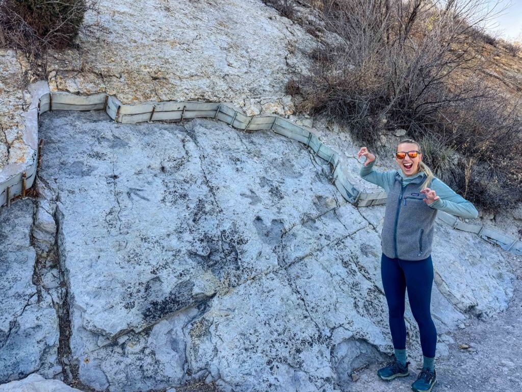 Smooth white rock surface with natural erosion patterns and cracks and a woman holding up her hands like a dinosaur