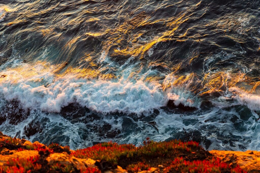 Waves crashing violently against jagged coastal rocks bathed in warm sunset light