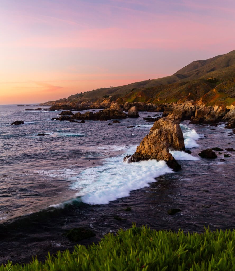 Purple twilight over a rugged coastline with a large sea stack rising from the sea