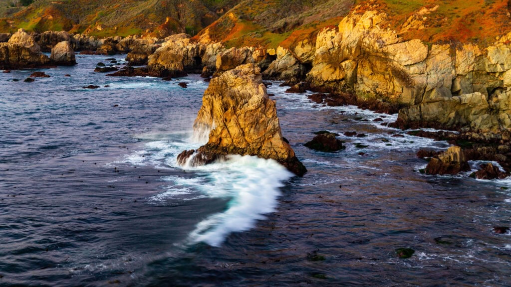 Sea stacks and crashing white surf along a rocky Big Sur coastline at dusk