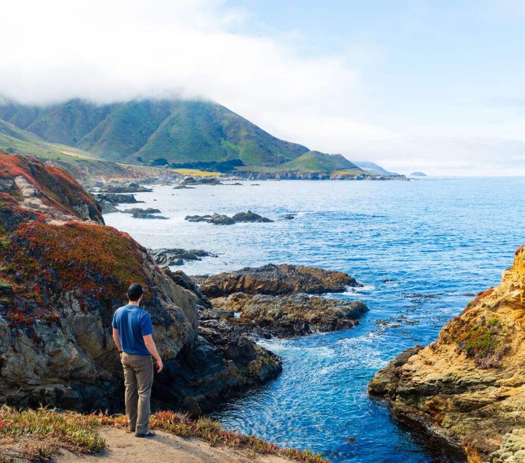 A rounded green hill rising above a bay with offshore fog and scattered rocks