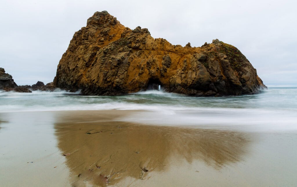 Weathered rock formations on a wide sandy beach with light surf