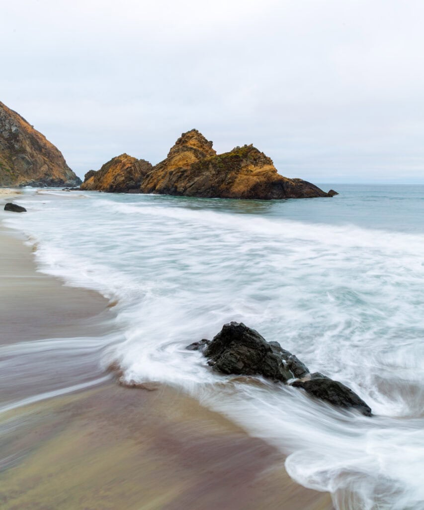 Sea stacks and a rocky bay with calm aquamarine water under overcast skies