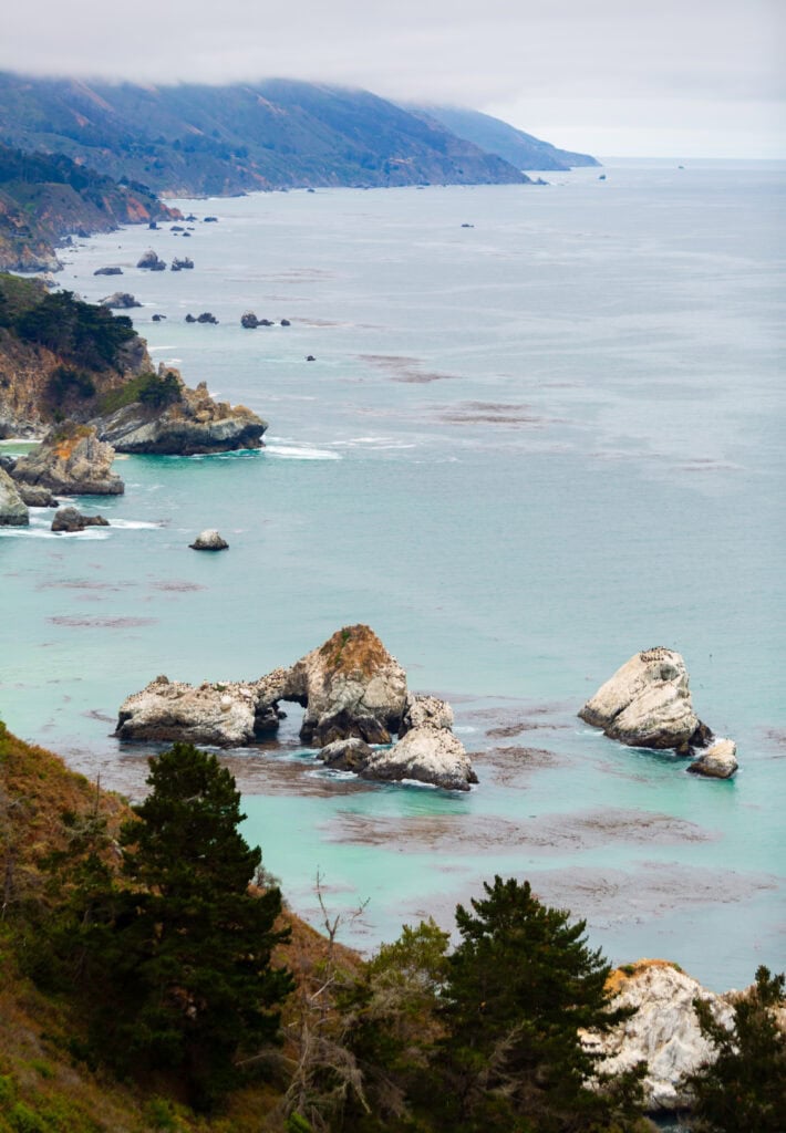 Sea stacks and a rocky bay with calm aquamarine water under overcast skies