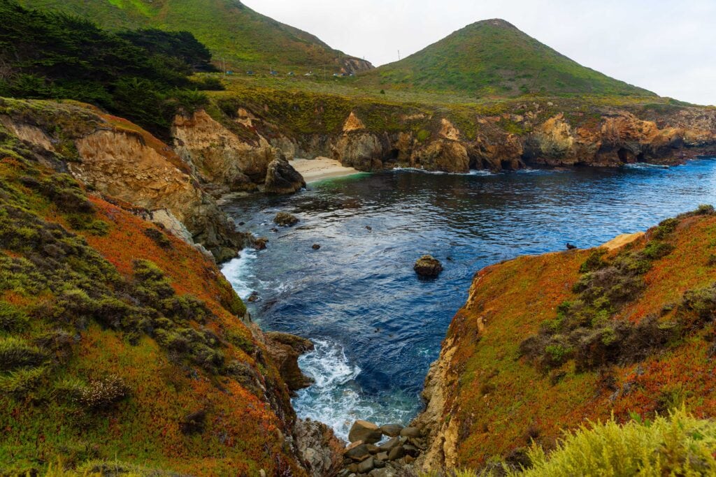 Lush green coastal hills rolling down to a rocky Big Sur shoreline