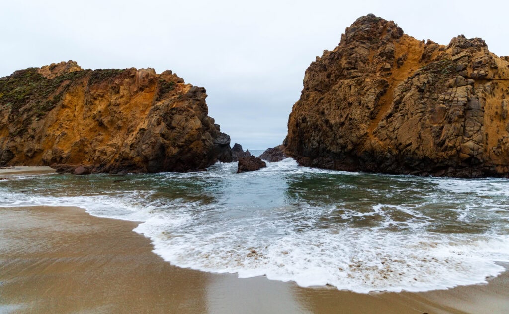 Two large sea stacks flanking a sandy cove on a calm gray day