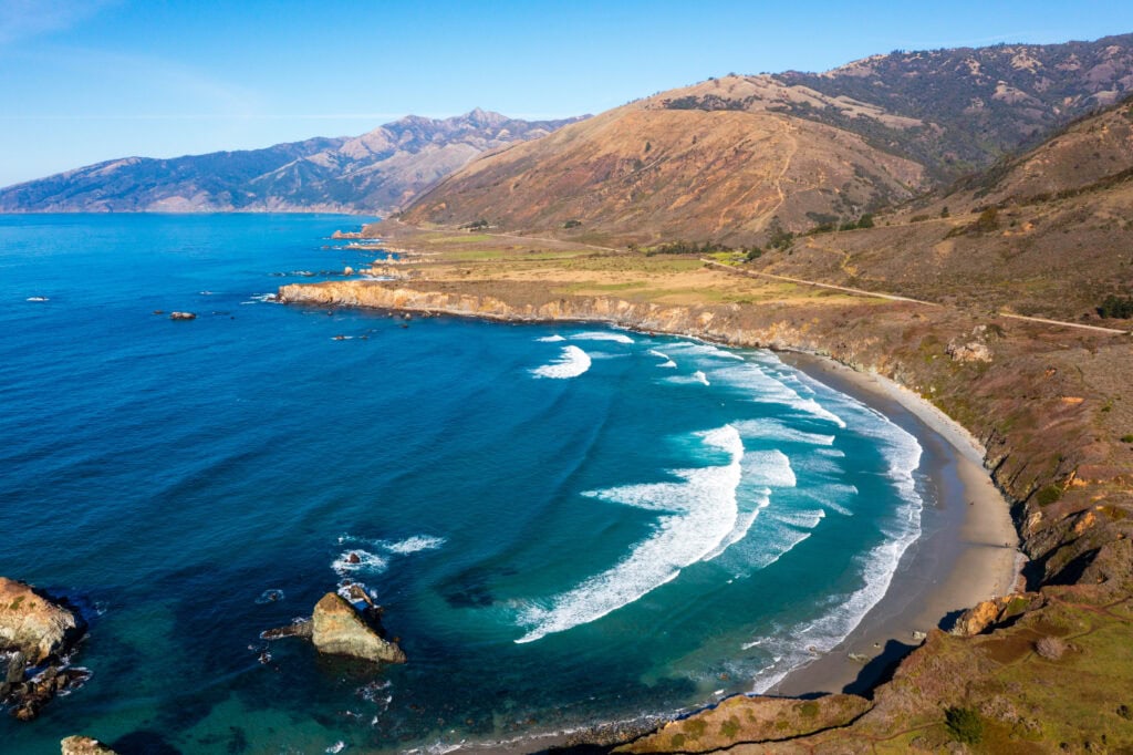 Aerial view of a sweeping curved bay with turquoise water and a sandy beach