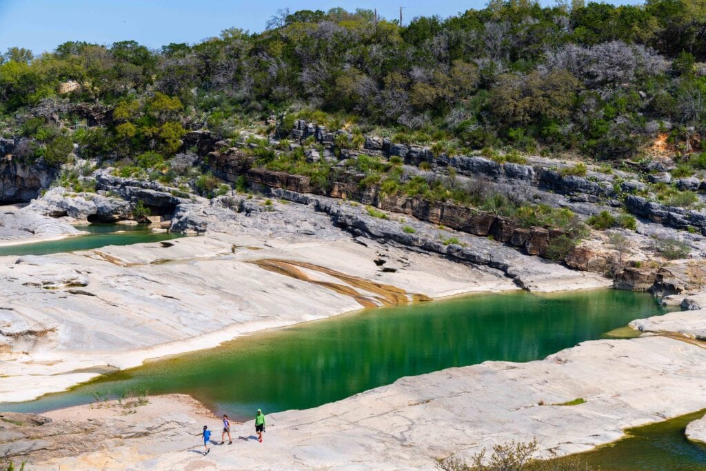 the pools at pedernales state park with three people walking at the bottom of the image