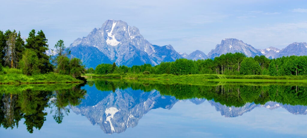 Broad view of the Teton Range reflected in a calm river or lake at midday
