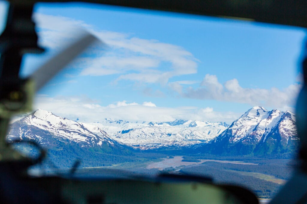 View from inside a small aircraft looking out over glaciated peaks and water