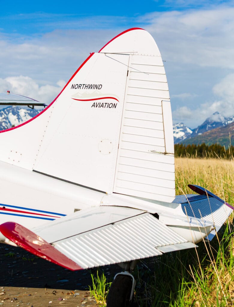 Small red-and-white bush plane on a gravel airstrip, mountains behind