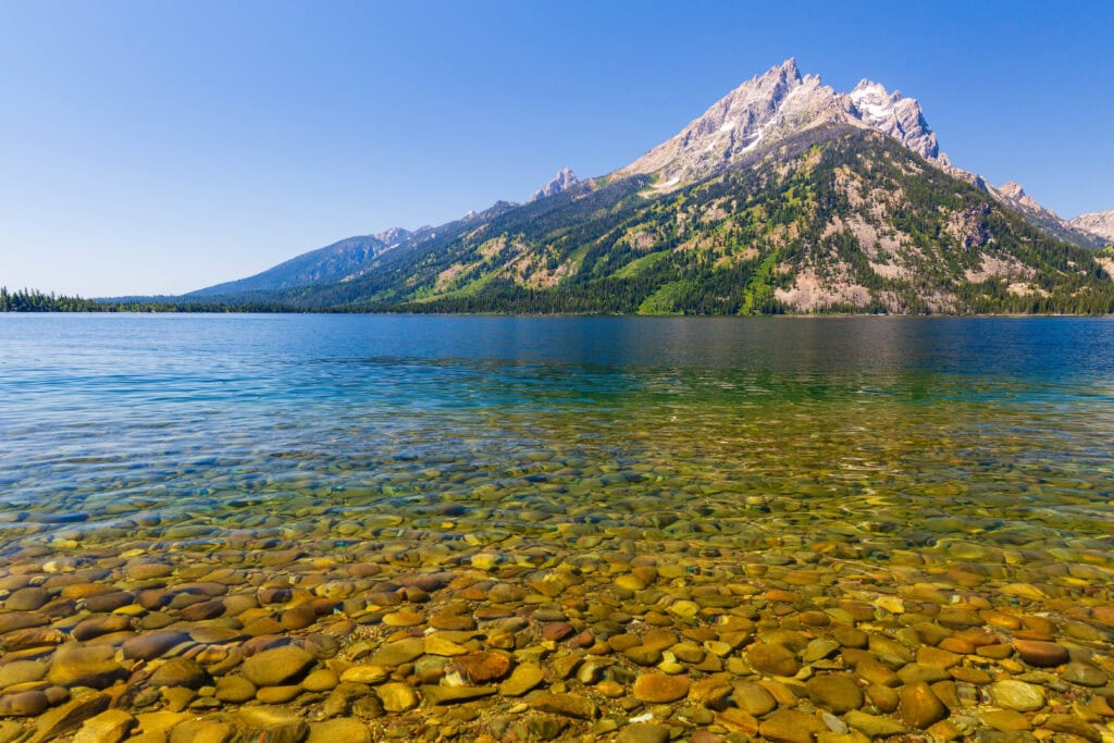 Crystal-clear shallow lake with rocky bottom and mountains in the distance