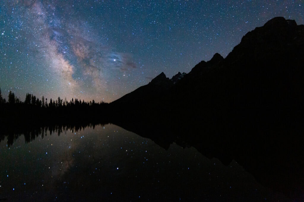 Dark silhouetted peaks beneath a bright starry sky with faint milky way glow