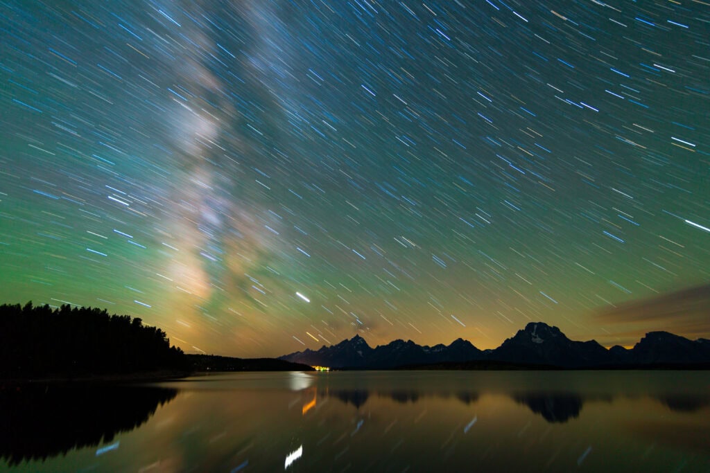 Milky Way galaxy arching over a dark mountain silhouette and still lake