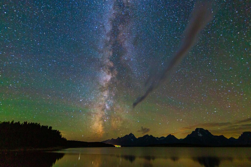 Milky Way galaxy arching over a dark mountain silhouette and still lake