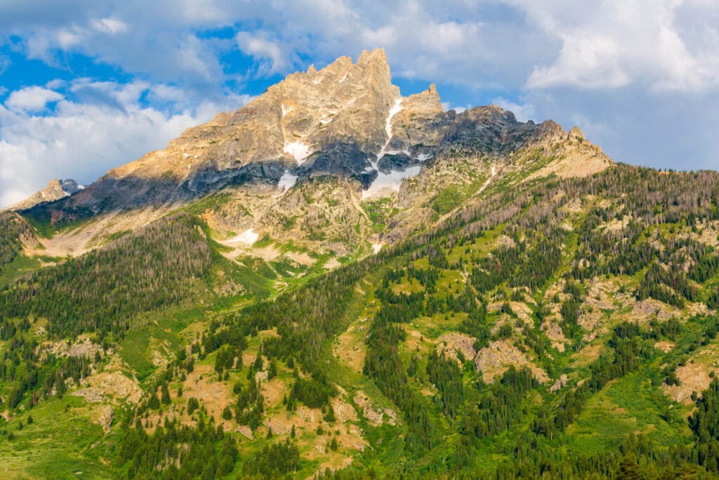 Snow-dusted mountain peak rising above a forested valley under blue sky