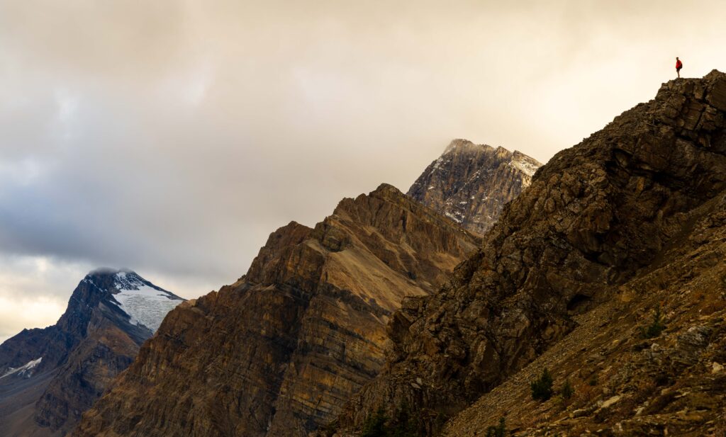 a hiker standing on a cliff on the jimmy simpson jr trail with taller mountains behind him