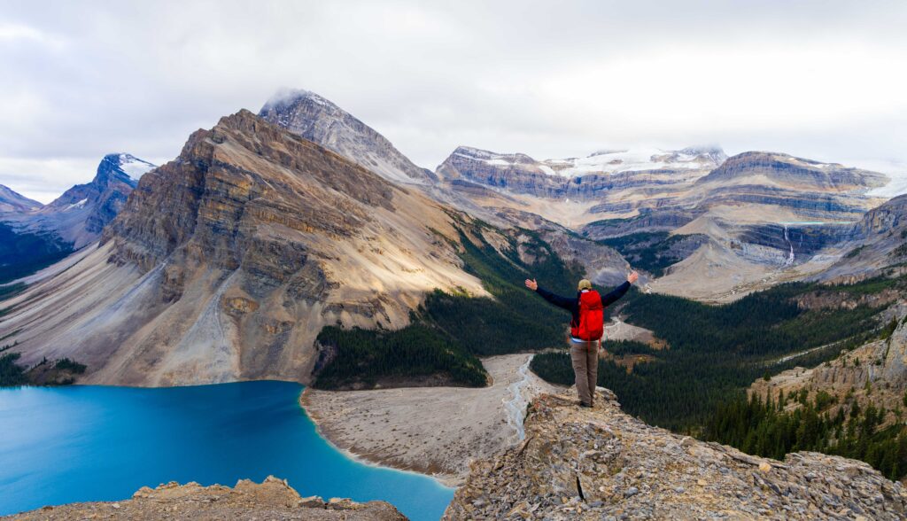 a single male hiker in a red backpack looks out over bow lake