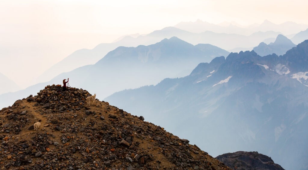 A steep rocky mountainside rises sharply against a backdrop of hazy blue peaks