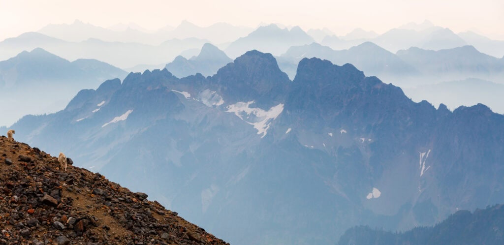 Layered blue mountain ridgelines recede into haze above a rocky alpine ridge
