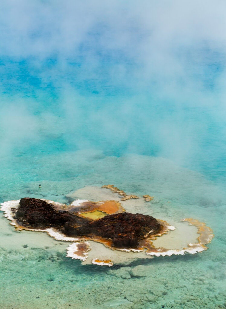 Turquoise hot spring with white mineral deposits and scattered pines
