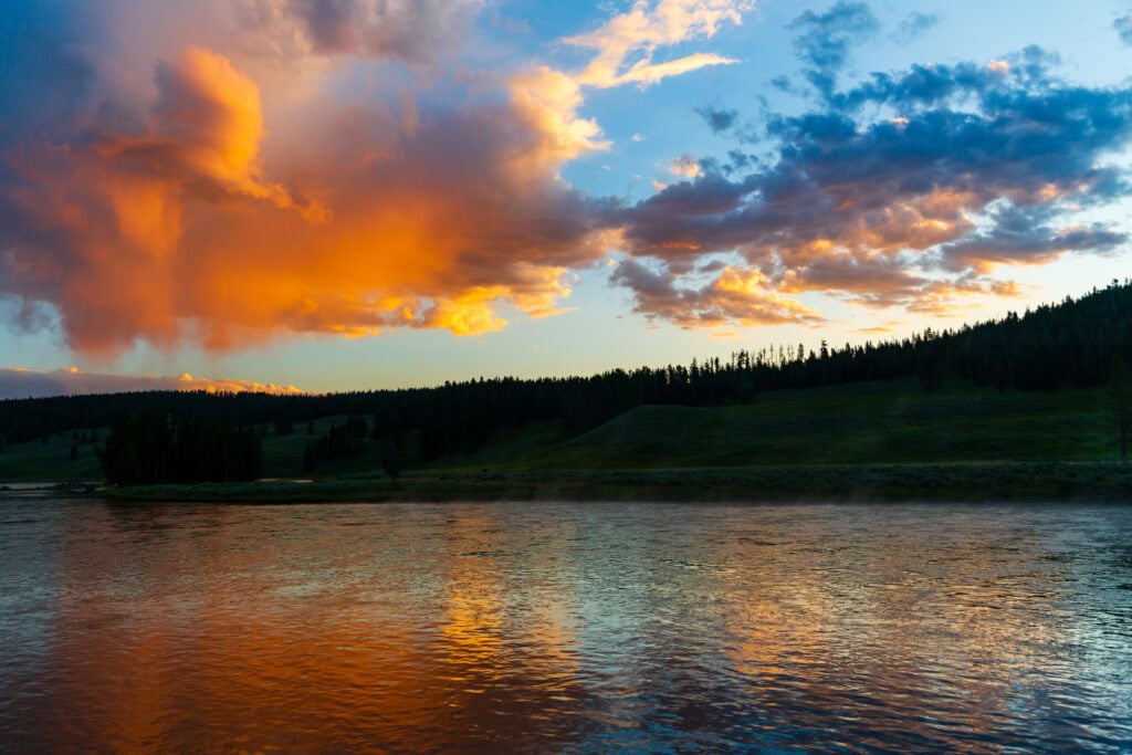 Orange and pink clouds reflected in a still Yellowstone lake at sunrise