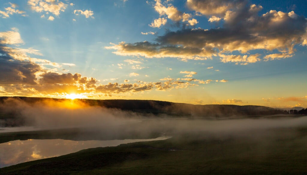 Golden sunrise over Yellowstone's rolling hills and silhouetted tree line