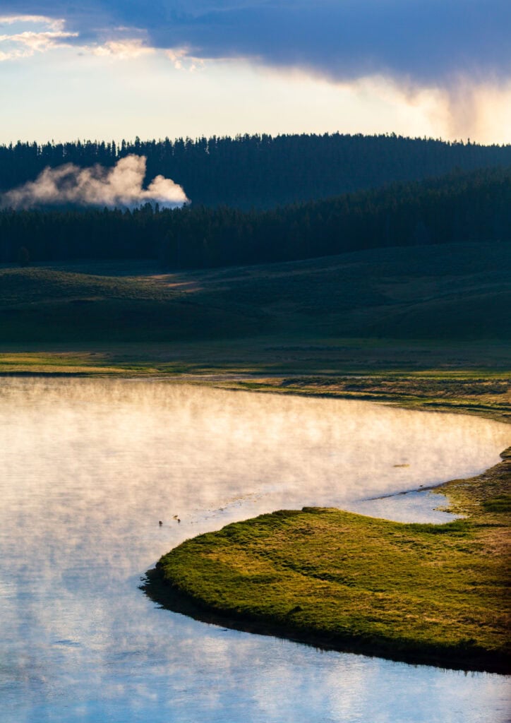 Meandering river through a flat valley with dark storm sky