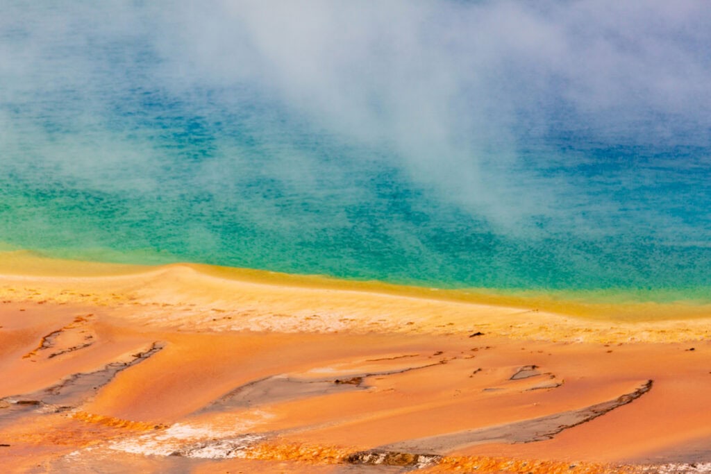 Orange and rust-colored bacterial mats along a hot spring's edge