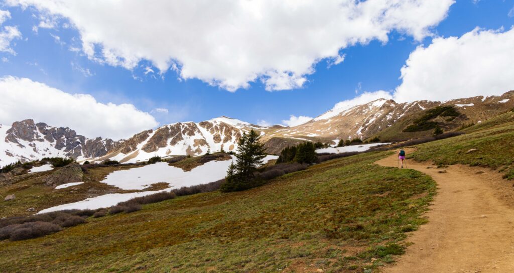 Trail winding through a snow-patched alpine basin below a rocky mountain ridge on Herman Gulch Trail