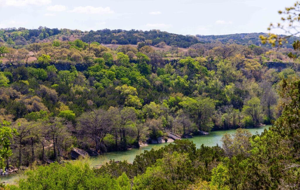 Aerial view of dense green forest and a winding river in Texas Hill Country near Westcave