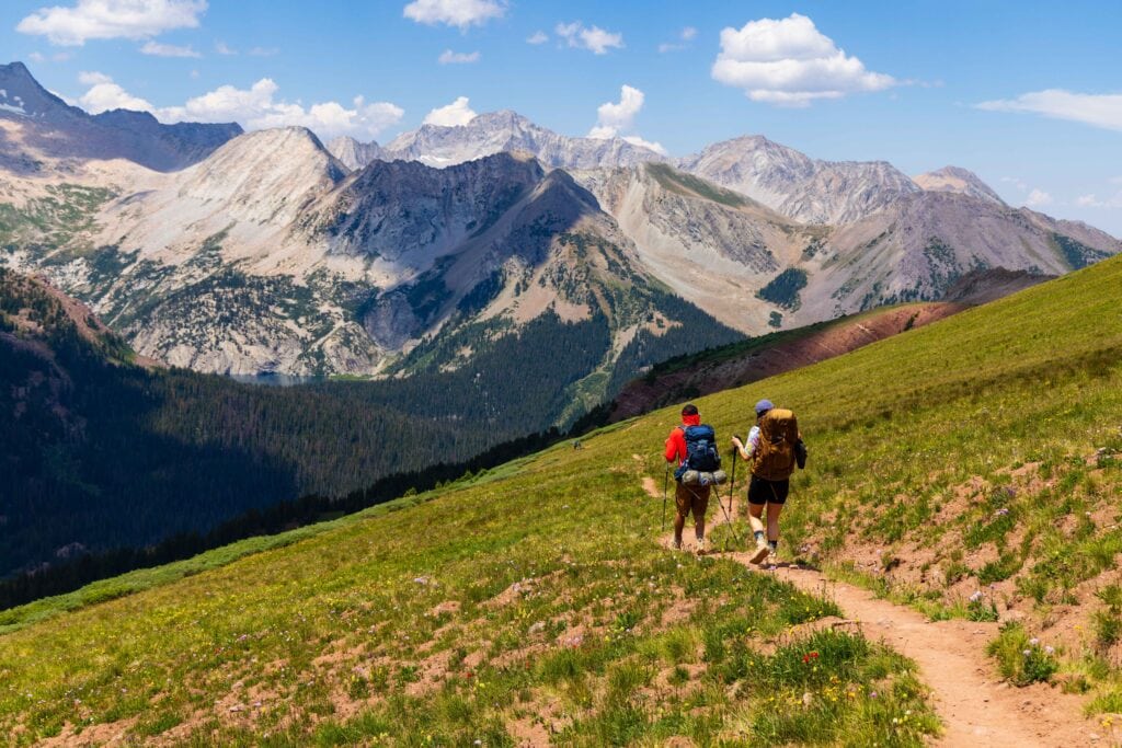 two hikers on the trail with mountains in the background, just leaving buckskin pass