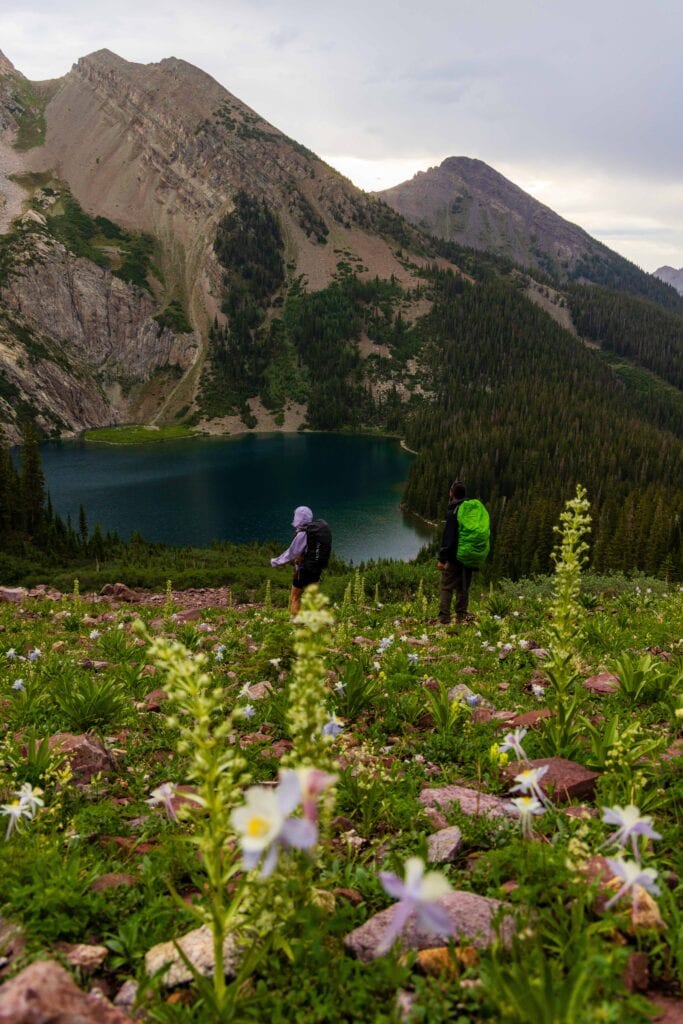 hikers on a trail in front of a lake and mountain