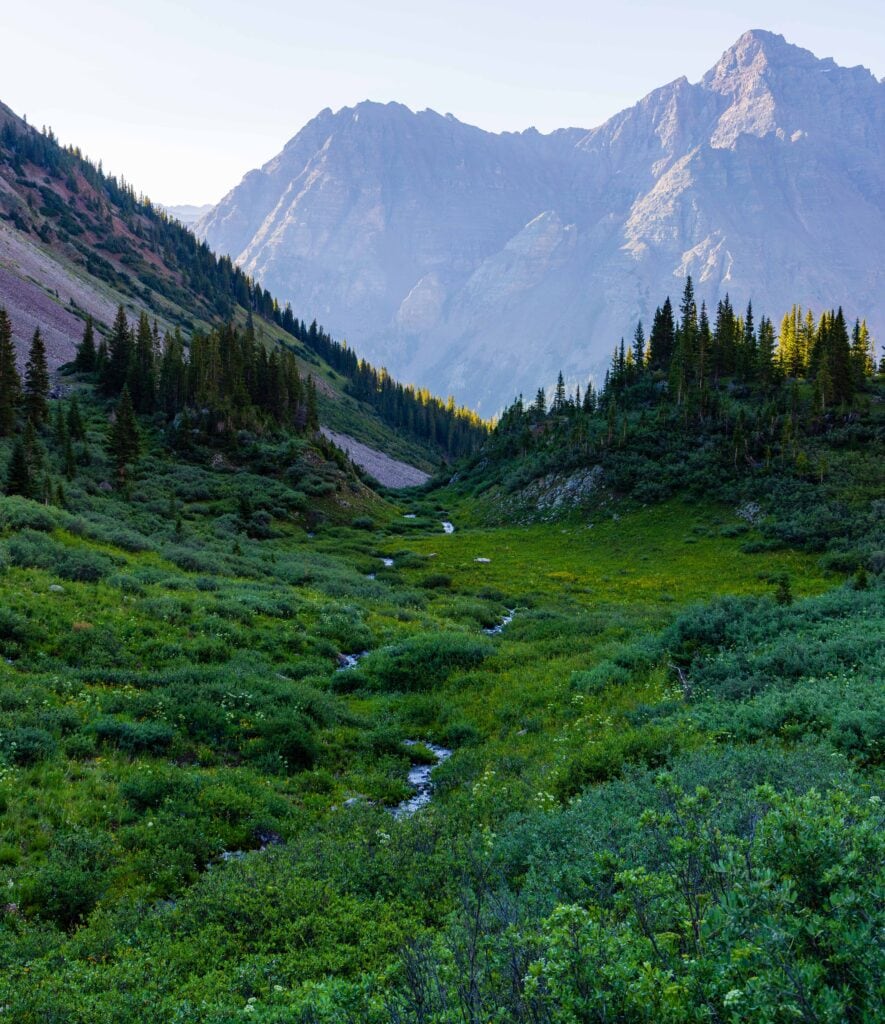 a green valley with mountains in the distance in the maroon bells