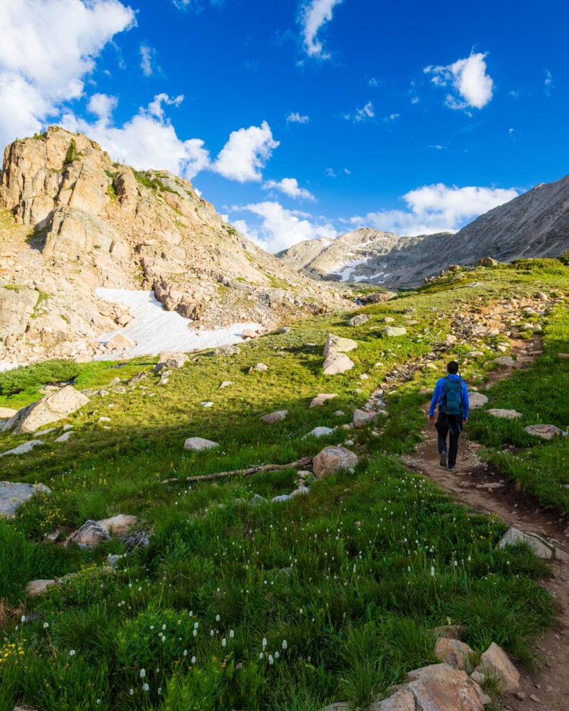 a hiker on a trail in colorados indian peaks wilderenss with a big mountain on the left hand side