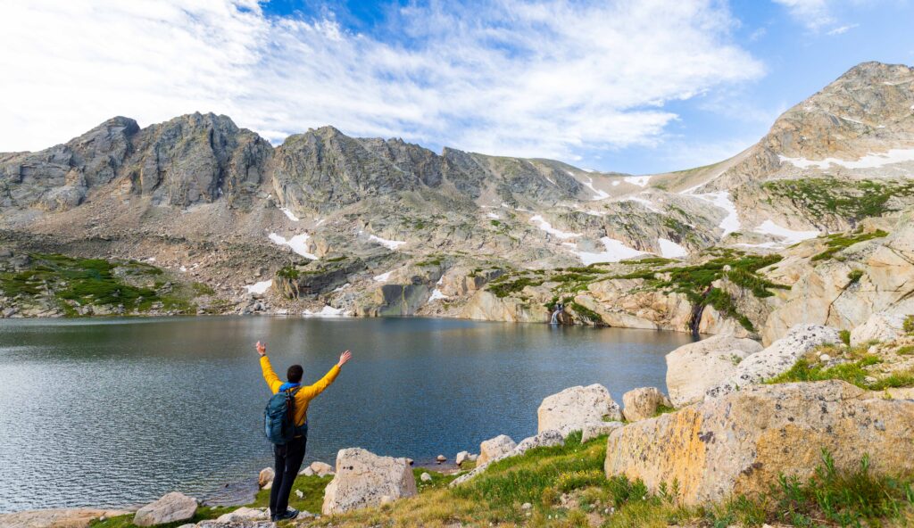 a hiker holds up his hands in front of blue lake in colorado's indian peaks wilderness