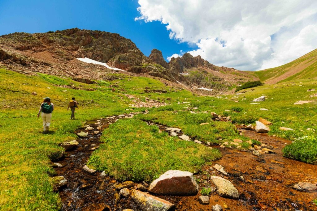 hikers traverse next to a creek in colorado