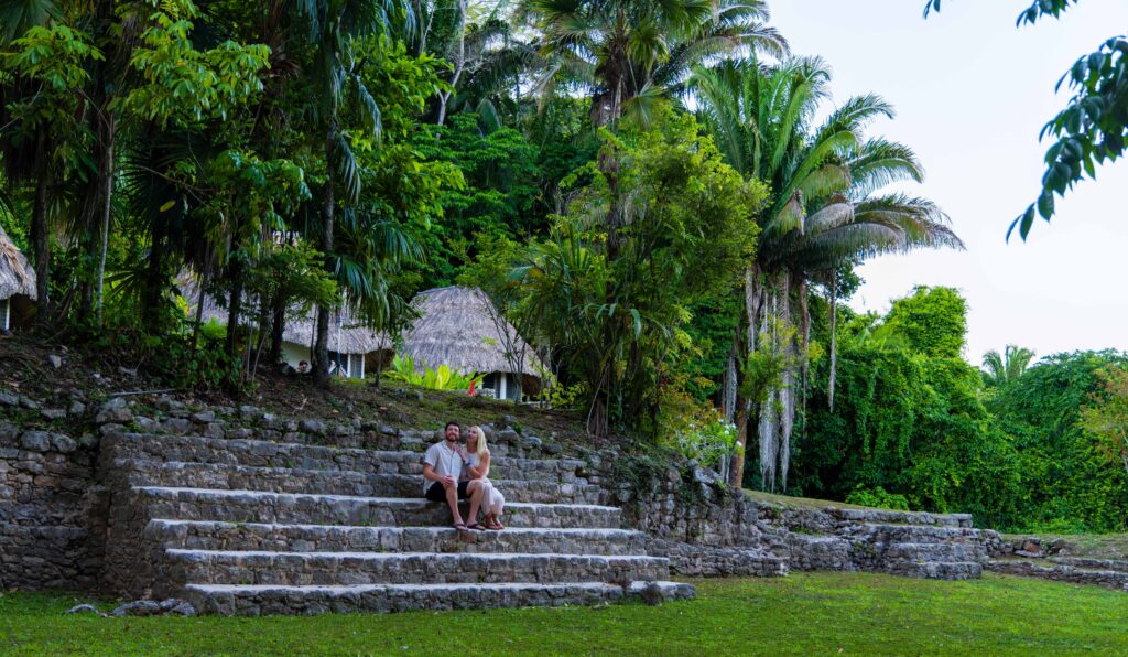 two people sit next to the mayan ruins at jade jungle resort