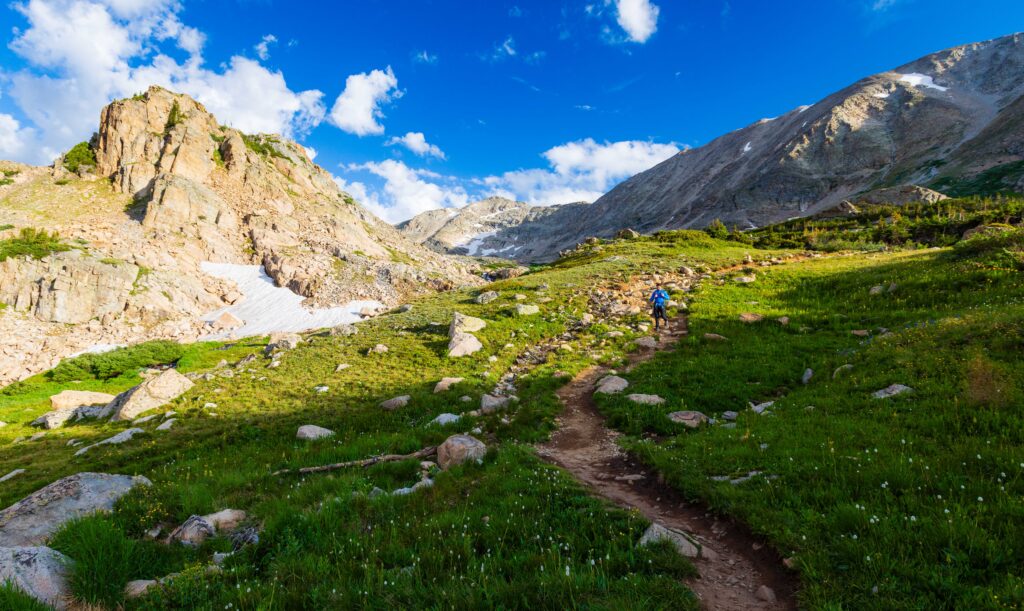 a hiker on a trail in colorados indian peaks wilderenss with a big mountain on the left hand side