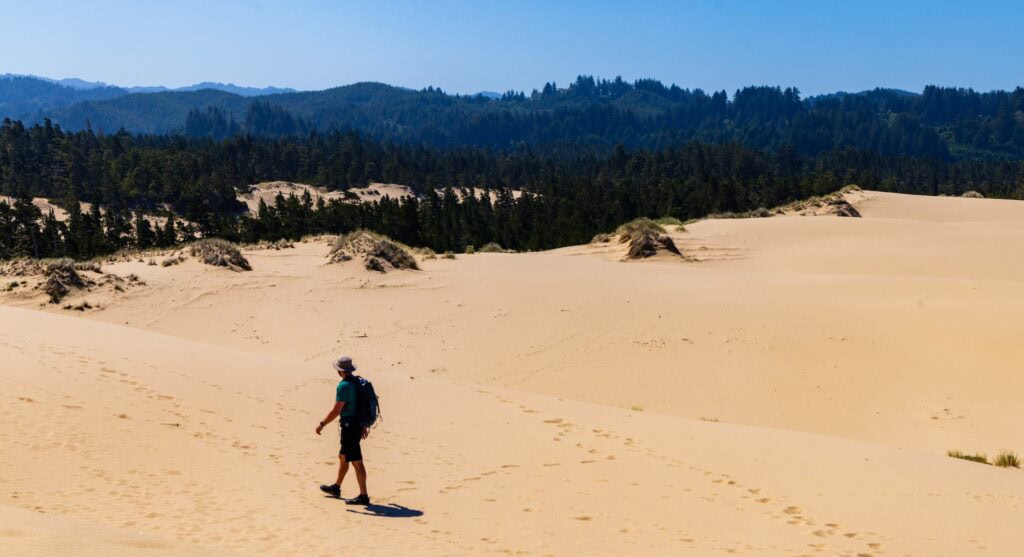 a hiker walking on the oregon dunes with blue sky